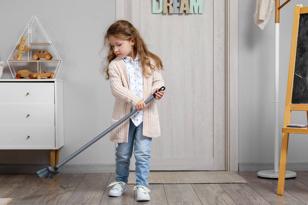 Cute little girl sweeping floor with broom at home - Фото, зображення