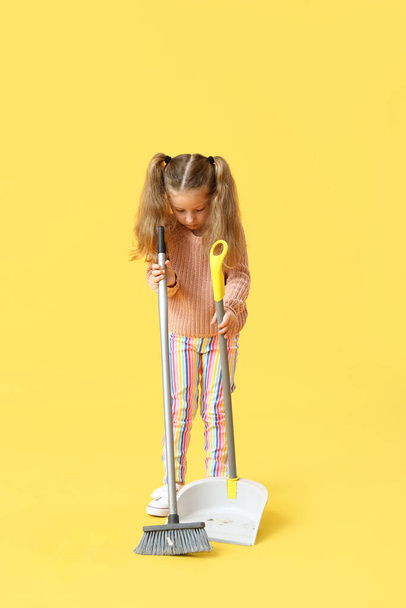 Милая маленькая девочка с метлой и совок на желтом фоне - Фото, изображение