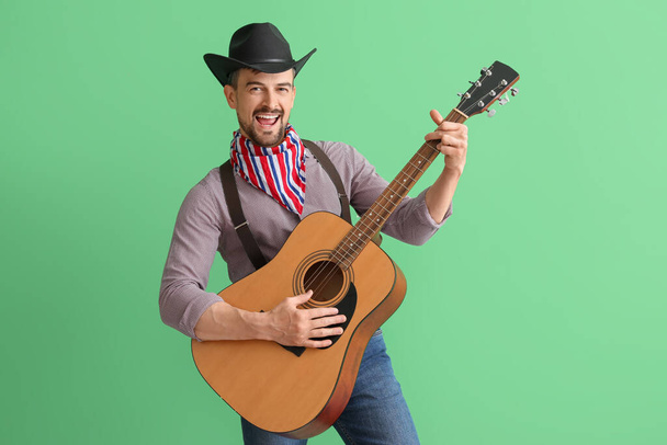Handsome cowboy playing guitar on green background - 写真・画像