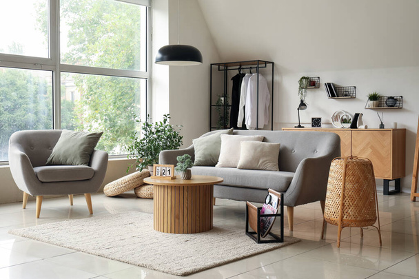 Интерьер светлой гостиной с серым диваном, креслом и деревянным журнальным столиком - Фото, изображение