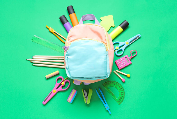 Color school backpack with different stationery on green background - Zdjęcie, obraz