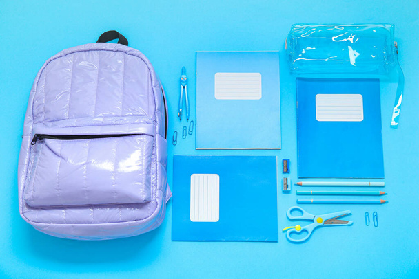 Lilac school rugzak met briefpapier op blauwe achtergrond - Foto, afbeelding