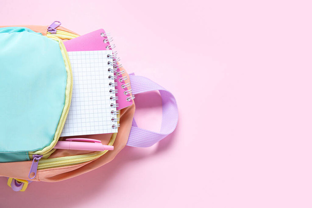Кольоровий шкільний рюкзак з канцелярськими приладами на рожевому фоні - Фото, зображення