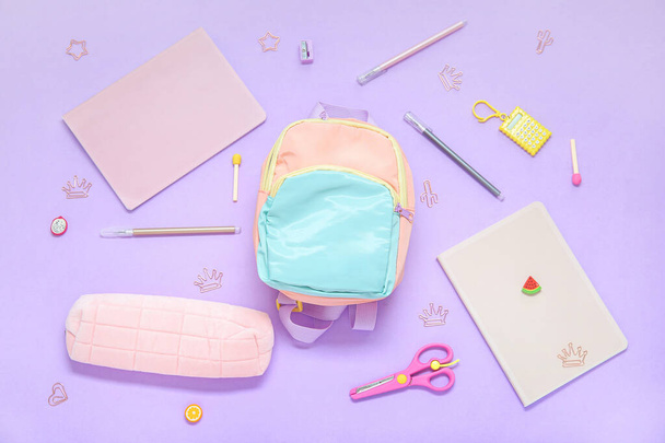 Color school backpack with different stationery on lilac background - 写真・画像