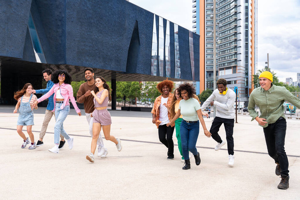 Happy playful multiethnic group of young friends bonding outdoors - Multiracial millennials students meeting in the city, concepts of youth, people lifestyle, diversity, teenage and urban life - Foto, imagen