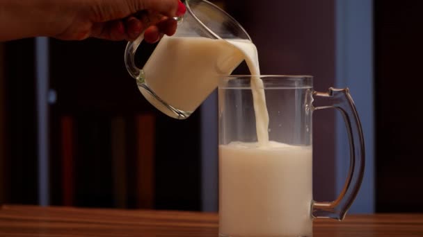 Milch, die von einer Person aus einem Krug oder einem anderen Glas in ein Glas gegossen wird - Filmmaterial, Video