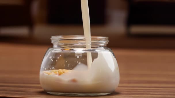 Słoik mleka i zbóż, wlewający mleko do szklanki i jogurt z suszonymi owocami - Materiał filmowy, wideo