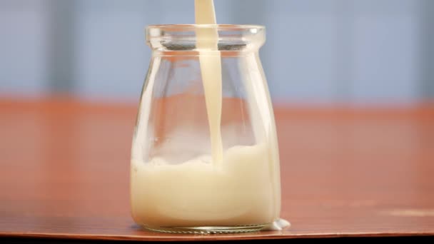En una mesa, hay un frasco de yogur, leche y crema. La leche se vierte en un vaso y un frasco con una cuchara. Otro vaso de leche también está allí. - Metraje, vídeo