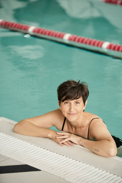 felice donna di mezza età con tatuaggio nuoto in piscina, al coperto, centro benessere, benessere, relax - Foto, immagini
