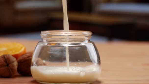 Un bocal à crème et un bocal à lait sur une table, le lait étant versé dans le bocal en verre - Séquence, vidéo