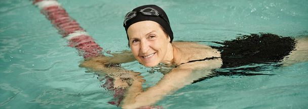 pozytywna kobieta w średnim wieku pływająca w basenie, czepek i gogle, patrząca w kamerę, sport, baner - Zdjęcie, obraz