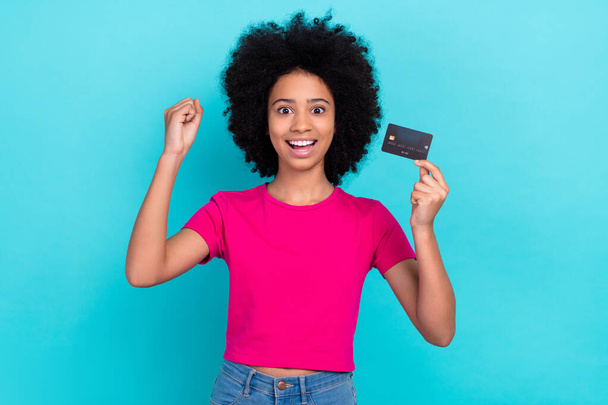 Photo of charming overjoyed girl with afro chevelure wear pink t-shirt hold credit card go shopping isolated on blue color background. - Fotó, kép