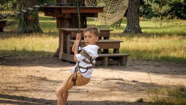 少年は森のサマーキャンプでジップラインに乗っている。アクティブな子供時代、健康的なライフスタイル、屋外で遊んでいる子供、自然の中で子供 - 写真・画像