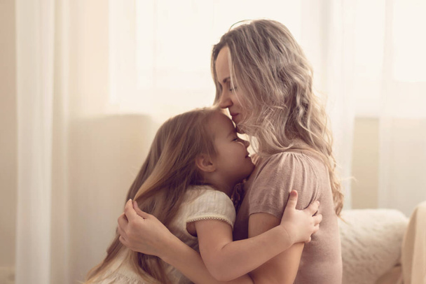 Smiling preschool girl sitting on mommies lap at home. Carefree mom and little girl laughing while playing at home. Love, warm family relationships. Happy kid with mum spending free time together. - Photo, Image
