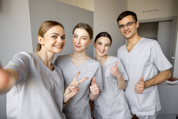 Νεαρή ομάδα νοσοκόμων που βγάζουν φωτογραφίες selfie, ενώ στέκονται μαζί στην ιατρική πτέρυγα. Πορτρέτο των χαρούμενων νοσοκόμων στην κλινική - Φωτογραφία, εικόνα