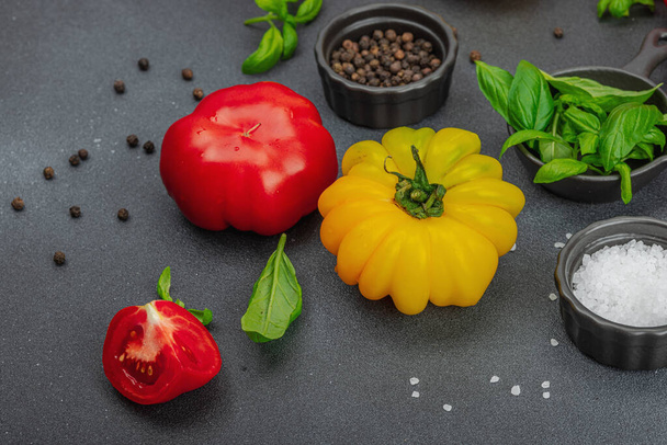 Kleurrijke Heirloom tomatenoogst. Rijp geribbelde groenten met verse basilicumbladeren. Sappig ingrediënt voor zomersla en specerijen. Zwarte stenen achtergrond, plat gelegd, close up - Foto, afbeelding