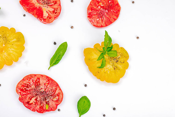 Farbenfrohe Tomatenernte isoliert auf weißem Hintergrund. Reifes Rippengemüse mit frischen Basilikumblättern. Saftige Zutat für Sommersalat und Gewürze, flach, von oben - Foto, Bild