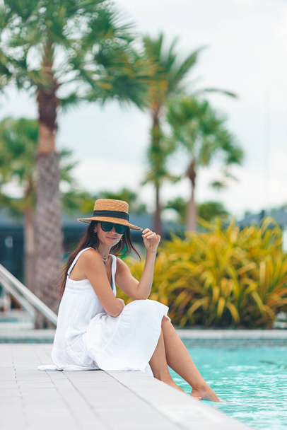 Επιστροφή άποψη της γυναίκας στο καπέλο χαλαρώνοντας από την εξωτερική πισίνα σε ένα πολυτελές ξενοδοχείο θέρετρο απολαμβάνοντας καλοκαιρινές διακοπές - Φωτογραφία, εικόνα