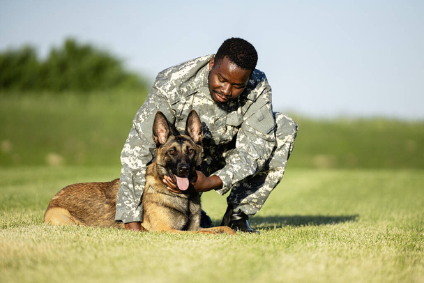 Στρατιωτικός σκύλος και ο στρατιωτικός διοικητής του απολαμβάνουν ελεύθερο χρόνο στο στρατόπεδο εκπαίδευσης. - Φωτογραφία, εικόνα