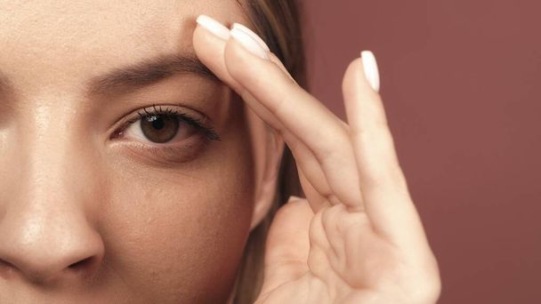 Cropped shot of a womans face in the studio on a pink background close up. A woman touches her eyebrows with her hand. Good vision and eye care. Contact lenses. Natural female beauty. Cosmetic line - Foto, Imagem