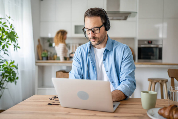 Un homme caucasien travail indépendant masculin de la maison avec des écouteurs sur sa tête sur ordinateur portable soutien à la clientèle pensée - Photo, image