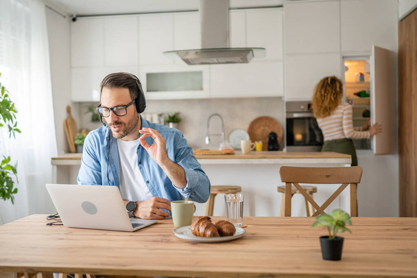 Um homem caucasiano masculino freelancer trabalho de casa com fones de ouvido na cabeça no laptop computador apoio ao cliente pensando - Foto, Imagem