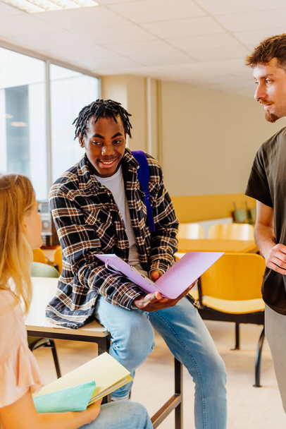 jonge zwarte man, student chats met zijn klasgenoten in de gangen van het instituut of universiteit tussen de klassen. Multiraciale groep studenten - Foto, afbeelding