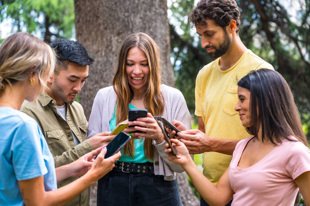 Multiethnic group with phones watching internet or social networks in the park, technology concept - Foto, Imagem