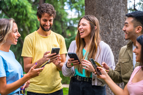 Multiethnic group smiling with phones on internet or social networks in the park, technology concept - Fotoğraf, Görsel
