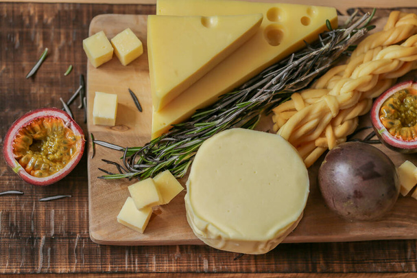 Käse sortiert geschnitten auf einem Holzbrett mit Kräutern und Früchten. Hart- und Weichkäse, Rosmarin und Maracuja. Mazdar Käsedreiecke, Gouda-Käsewürfel, Chechil geräuchert. Milchfett und Milchprodukte.  - Foto, Bild