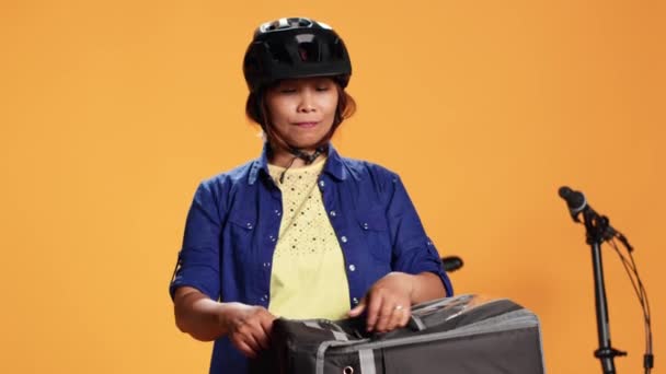 Közelkép futár nő elszigetelt narancssárga stúdió háttér hozza pizza ügyfél. Ázsiai kerékpáros szállít elvitelre élelmiszer az ügyfél, figyelembe étkezési dobozok termikus táska - Felvétel, videó