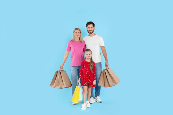 Happy family with shopping bags on light blue background - Foto, Bild
