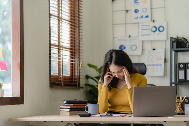 Азиатская деловая женщина, испытывающая напряжение глаз и жаждущая спать за столом в офисе, работая с ноутбуком или ноутбуком. - Фото, изображение