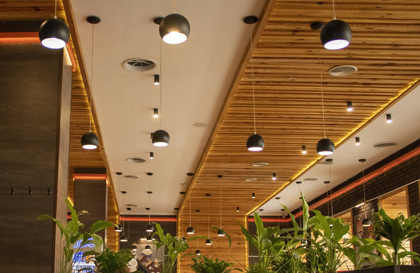 Sala iluminada en un café. Techos de madera marrón con lámparas modernas colgantes en un café o restaurante. - Foto, imagen