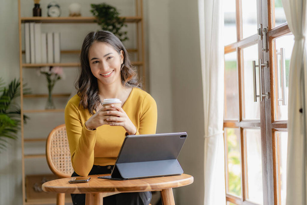 Azji freelance kobieta swobodnie trzymając kubek kawy pracy z tabletem do surfingu internetowego i blogowania w kawiarni stylu życia biznesu - Zdjęcie, obraz