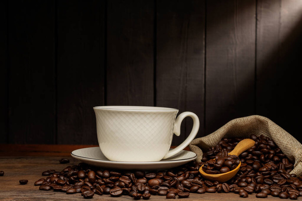 weiße Kaffeetasse mit schwarzem Kaffee oder heißem Tee in einer Cappuccino-Espresso-Tasse Frühstück mit Kaffeebohnen auf Holztisch isoliert auf schwarzem Hintergrund - Foto, Bild