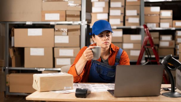 お茶やコーヒーを飲む女性マネージャーは小包の棚の列,出荷の準備ができているパッケージで倉庫の貯蔵庫で働いています. 仕事で休憩する. コピースペース - 写真・画像