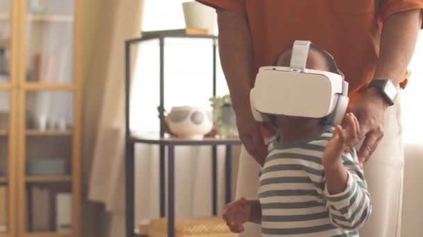 Μικρή Αφρο-Αμερικανίδα που περπατάει στο σαλόνι με τον πατέρα της φορώντας ακουστικά VR. - Πλάνα, βίντεο