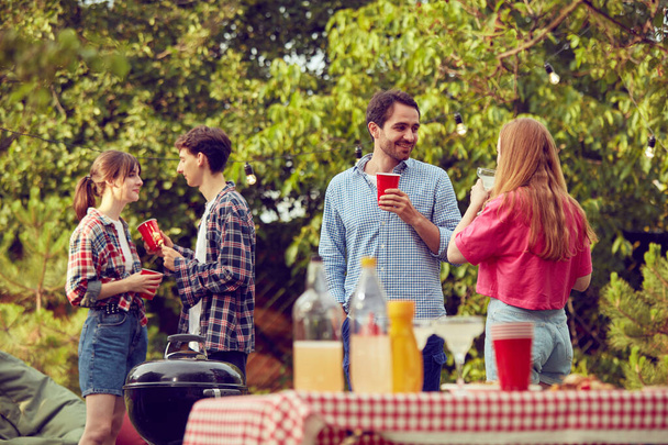 Young people, friends, couples spending good time together outdoors on warm day, doing barbecue, drinking cocktails. Concept of friendship, leisure time, weekends, summer, party, nature - 写真・画像