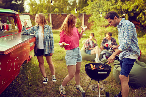 Group of young people, friends spending time outdoors, having barbecue party, cooking, drinking cocktails, talking. Countryside meeting. Concept of friendship, leisure time, weekends, summer, party - Fotoğraf, Görsel