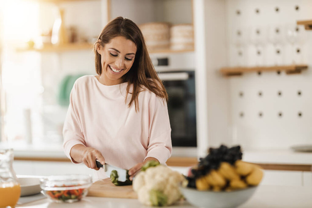 Фотография молодой женщины, рубящей овощи и готовящей здоровую еду на кухне. - Фото, изображение