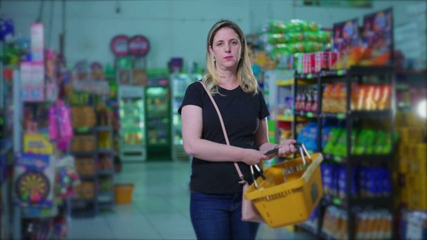 Retrato de cerca de la cesta de consumo femenina seria en el supermercado, mujer caucásica dentro de la tienda de comestibles, que representa los hábitos de estilo de vida de consumismo durante los tiempos negativos - Foto, imagen