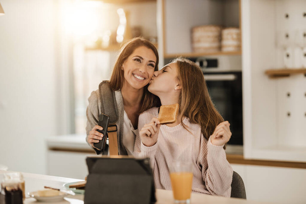 schattig tiener meisje en haar glimlachende moeder is begroeten elkaar in haar huis terwijl mam klaar om te gaan werken. - Foto, afbeelding