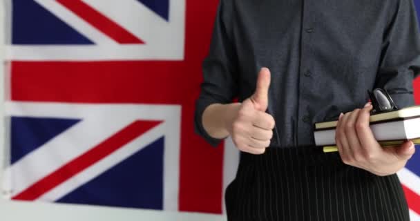 Жінка тримає підручники з прапора Великобританії і показує великі пальці вгору. Вища освіта в Англії для іноземців - Кадри, відео