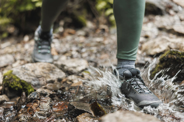 Foto ritagliata di una donna escursionista irriconoscibile che attraversa un ruscello mentre esplora nel bosco. - Foto, immagini