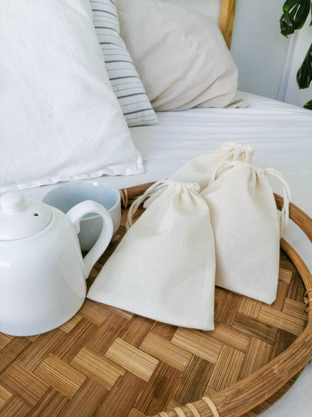 Бавовняні сумки на бамбуковому підносі в готельному номері з білим ліжком. Високоякісна фотографія - Фото, зображення