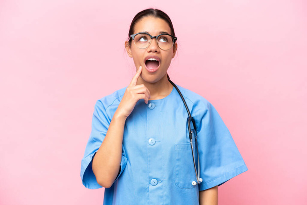 Junge Krankenschwester kolumbianische Frau isoliert auf rosa Hintergrund denken eine Idee zeigt mit dem Finger nach oben - Foto, Bild