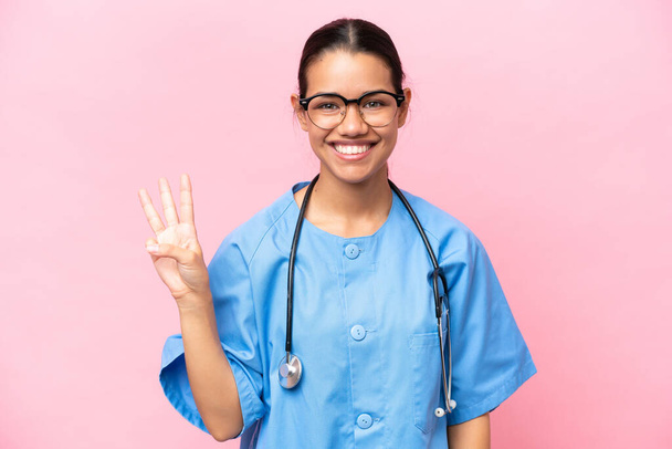 Joven enfermera colombiana aislada sobre fondo rosa feliz y contando tres con dedos - Foto, Imagen