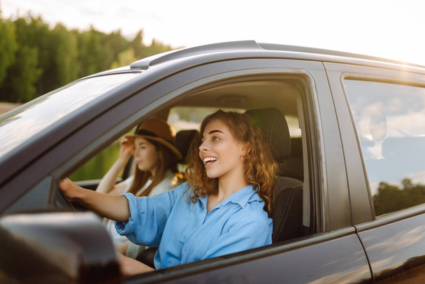 Retrato de dos mujeres jóvenes en un viaje en coche divirtiéndose, sonriendo, charlando juntas, disfrutando de la naturaleza. Estilo de vida activo, viajes, turismo, naturaleza. - Foto, Imagen
