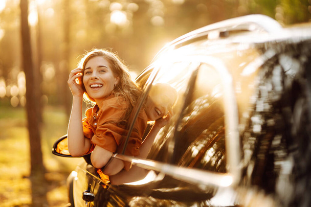 Feeling of freedom on beautiful sunny summer road. Shot of an attractive woman leaning out of car window while driving. Active lifestyle, travel. - Foto, afbeelding